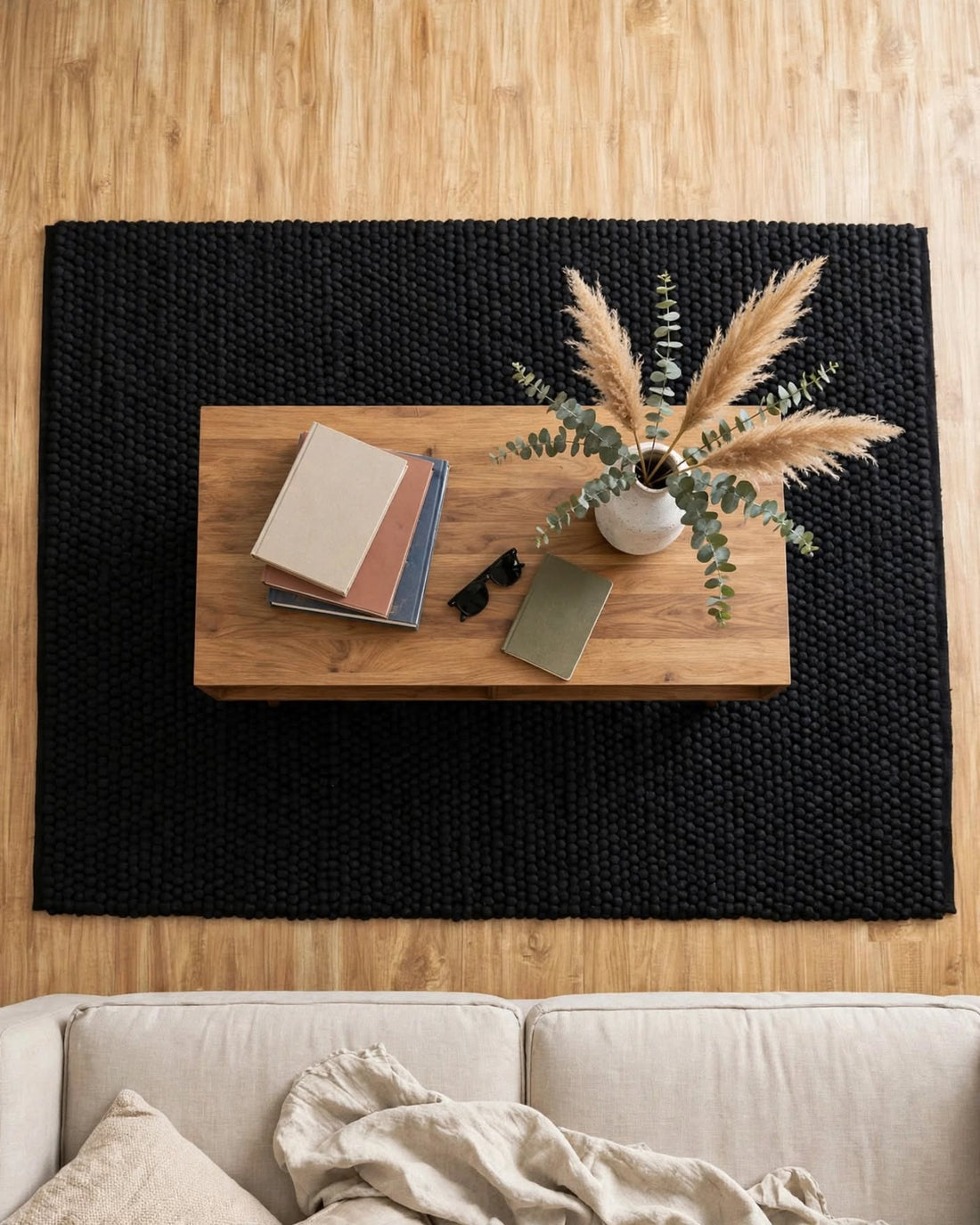 Charcoal Black Chunky Wool Area Rug, handmade in Bhadohi India – a large black woven area rug laid on a light wood floor, styled with a wooden