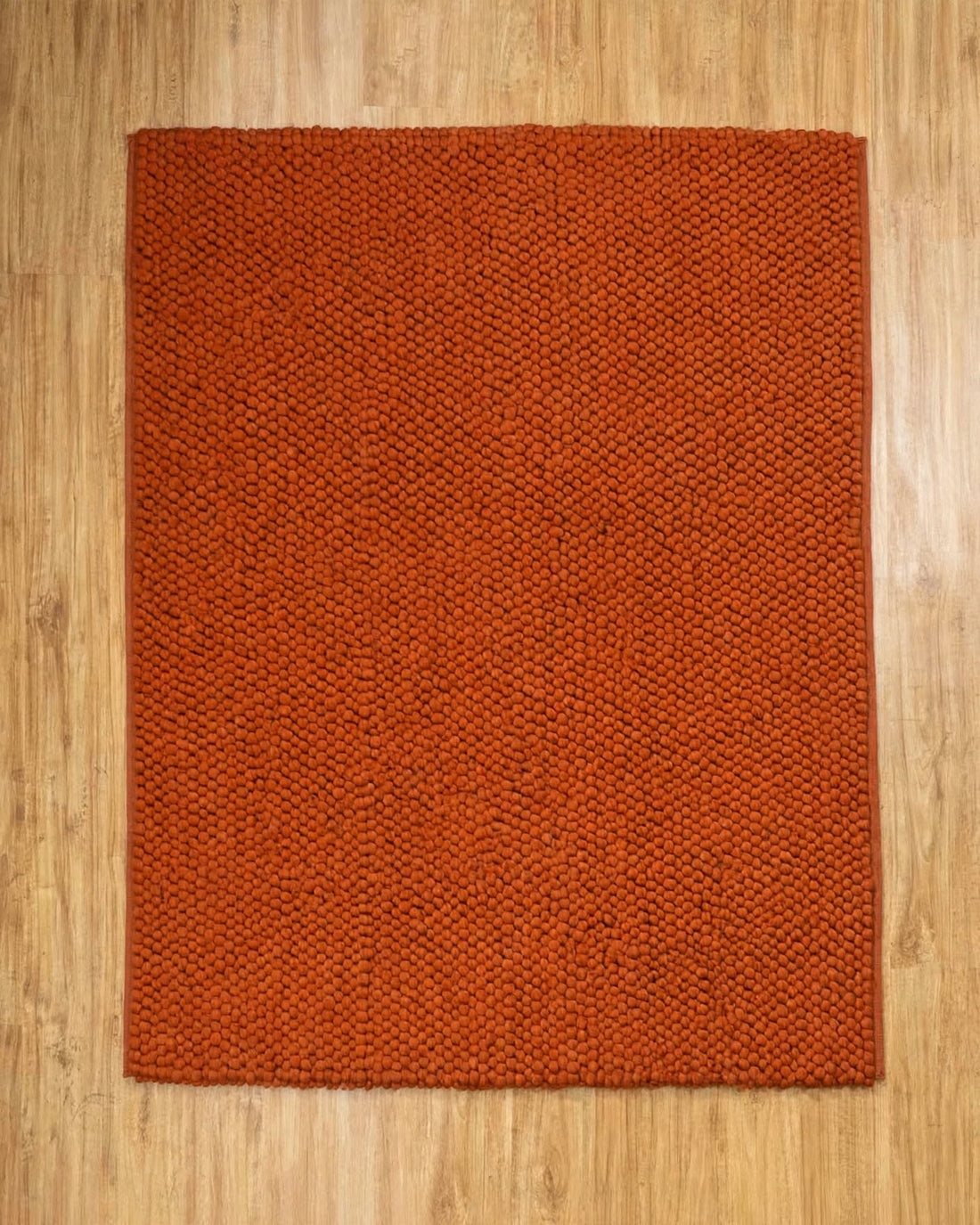 Terracotta Rust Chunky Wool Area Rug, handmade in Bhadohi India – a rectangular rust-orange woven rug with a textured, basketweave-like pattern,
