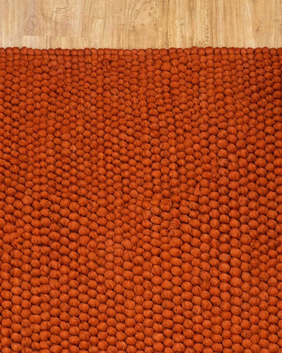 Terracotta Rust Chunky Wool Area Rug, handmade in Bhadohi India – a close-up of a textured orange-brown area rug with a raised, pebble-like